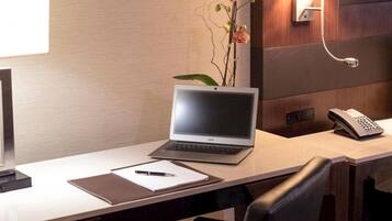 Una habitación de hotel con una computadora portátil sobre un escritorio, un teléfono, un bloc de notas y un bolígrafo.