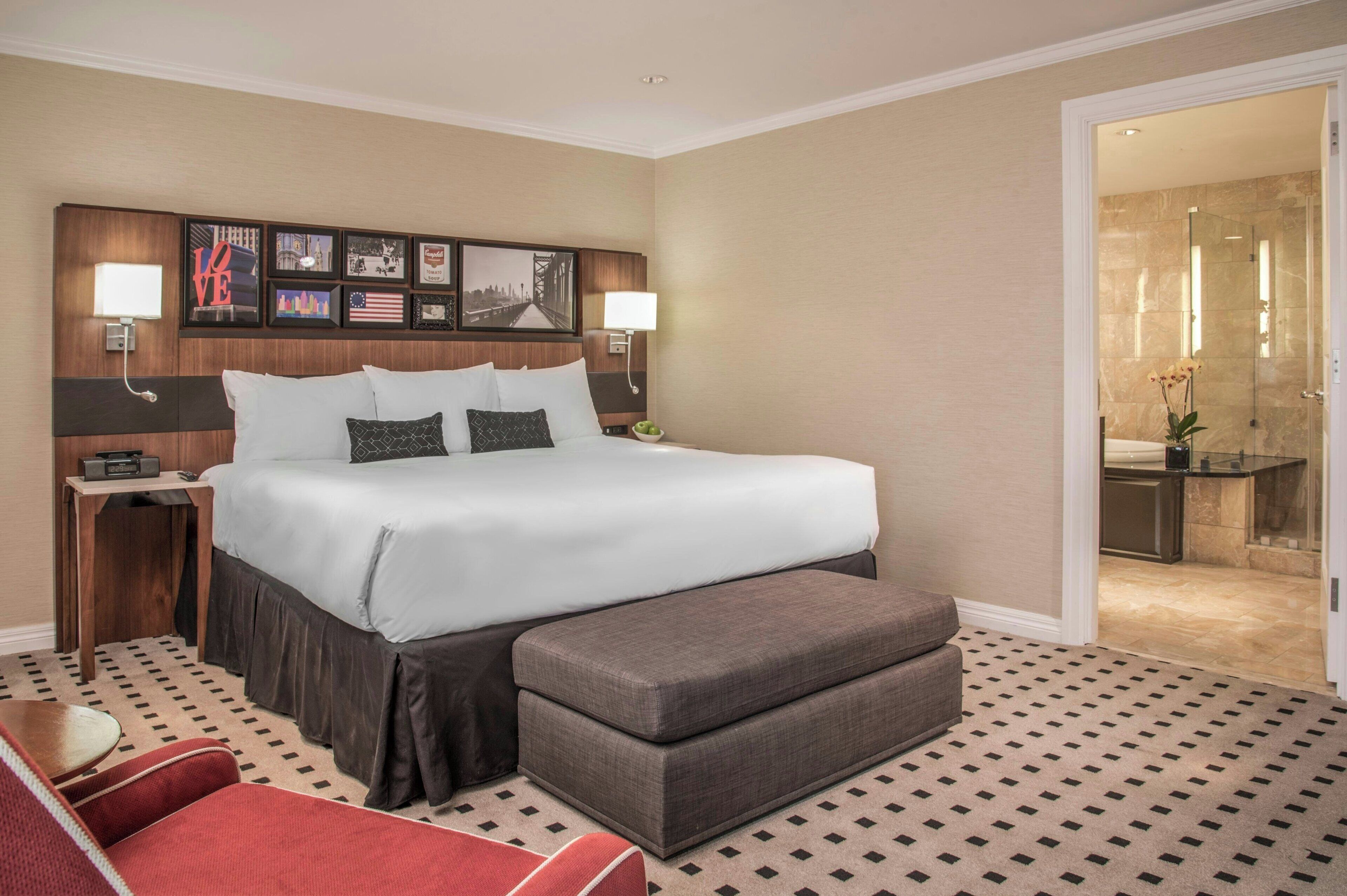 Een hotelkamer met een groot bed, nachtkastjes, een rode fauteuil en een badkamer die door een open deur zichtbaar is.