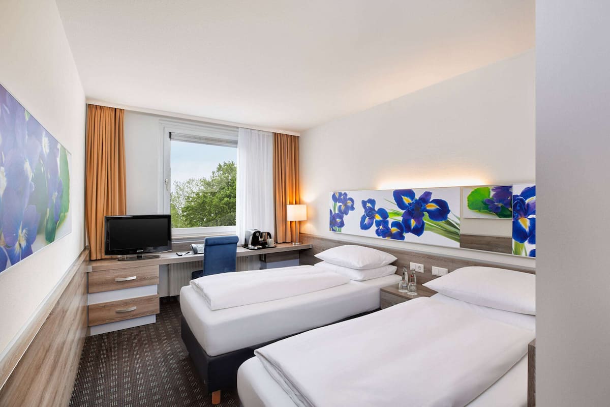 A hotel room with two beds, a desk with a computer, a TV, and a window with curtains.