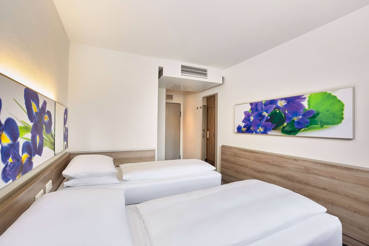 A hotel room with two beds, a wooden headboard, and a large floral artwork on the wall.