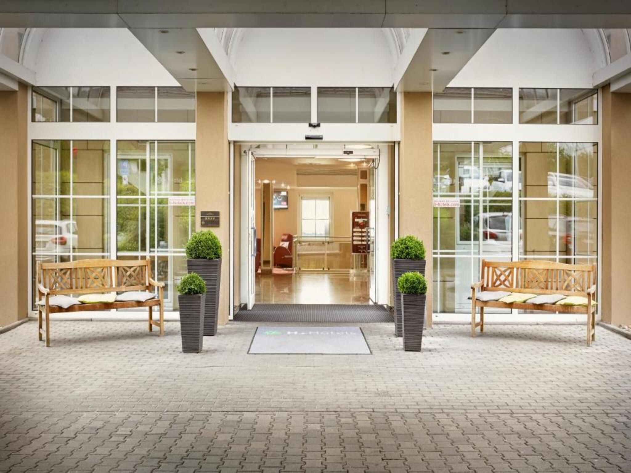 A hotel entrance with a reception desk, two benches, and potted plants.
