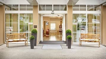 A hotel entrance with a reception desk, two benches, and potted plants.