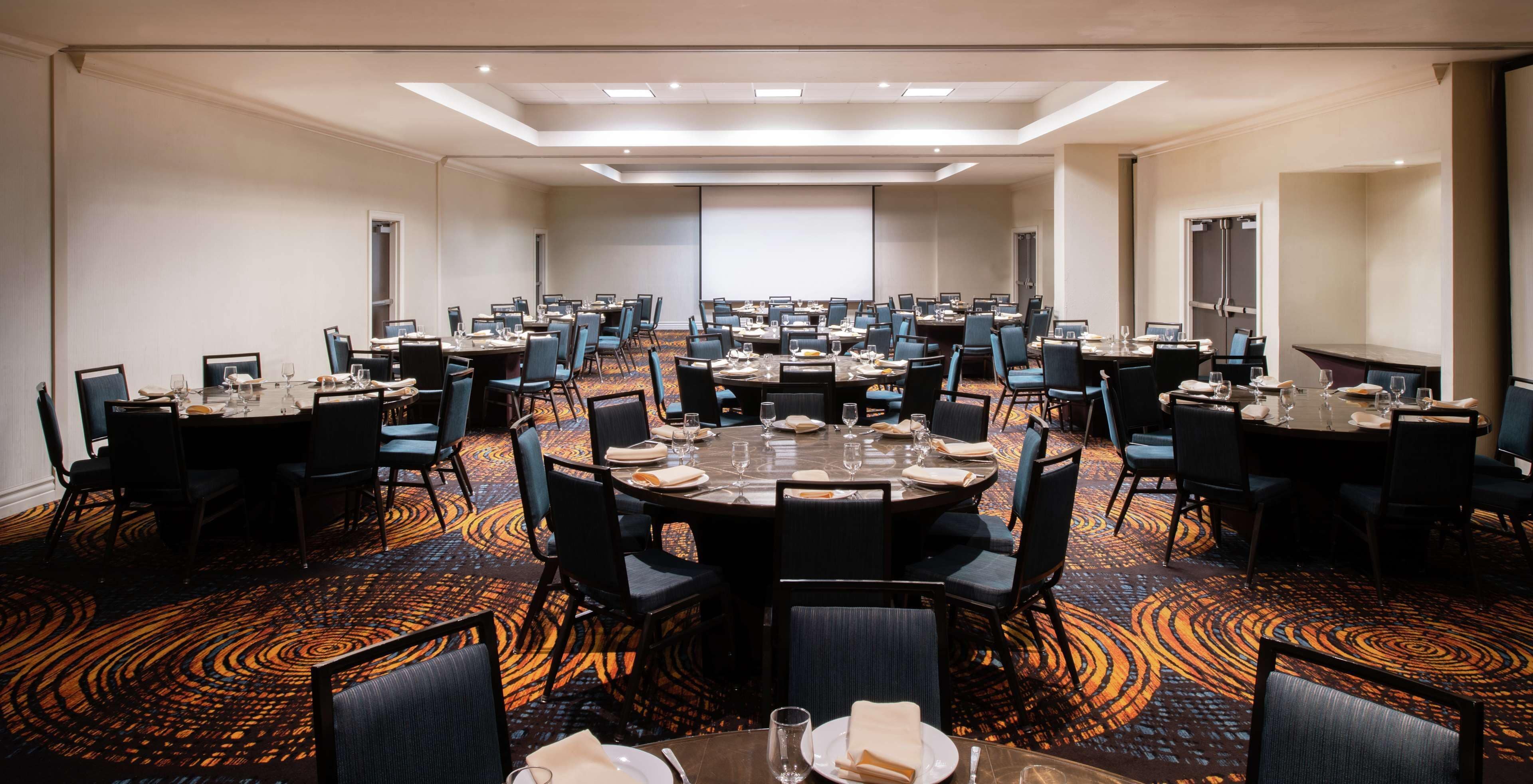 A large conference room with multiple round tables, each set with plates, glasses, and chairs.