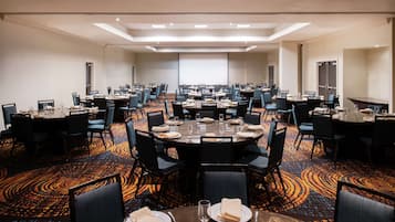 A large conference room with multiple round tables, each set with plates, glasses, and chairs.
