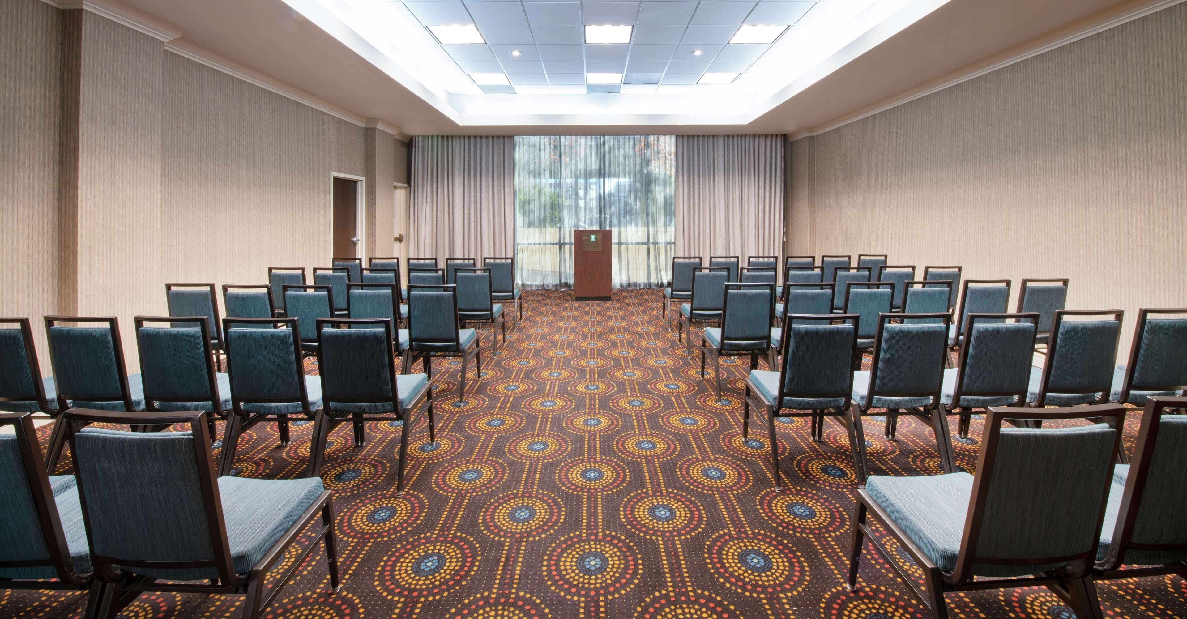 A conference room with rows of chairs, a podium, and a patterned carpet.