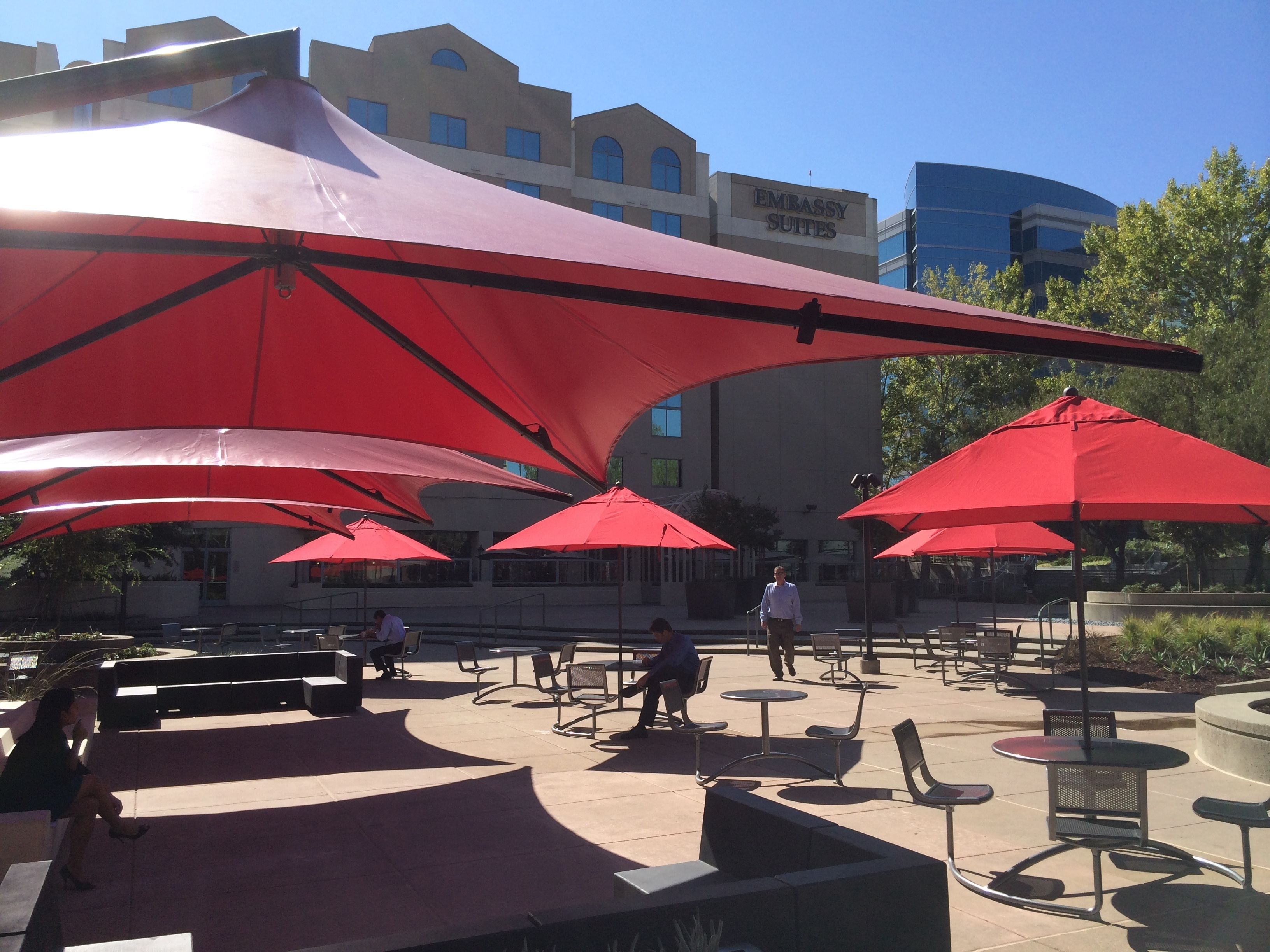 An outdoor seating area with red umbrellas, tables, and chairs.