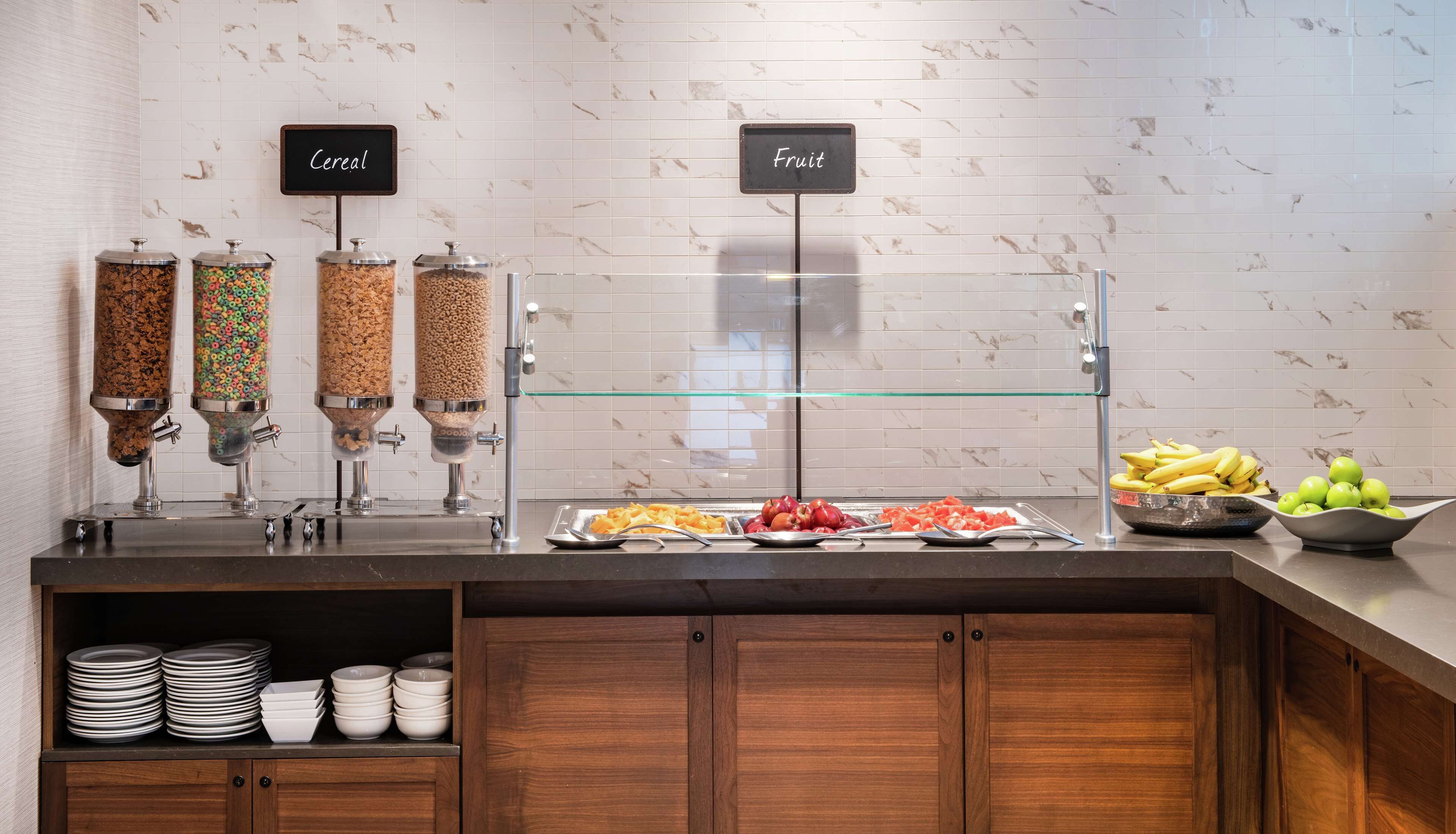Un área de bufé con dispensadores identificados para cereales y fruta, así como una variedad de frutas y cereales en la barra.