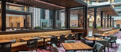 A modern hotel lobby with a seating area, a bar with a wine display, and a view of the building's exterior.