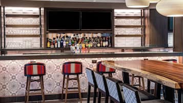 A bar area with a wooden counter, multiple stools, and a television screen.