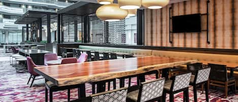 Een moderne vergaderruimte met een lange houten tafel, gestreept stoelen en een opvallende plafondlamp.