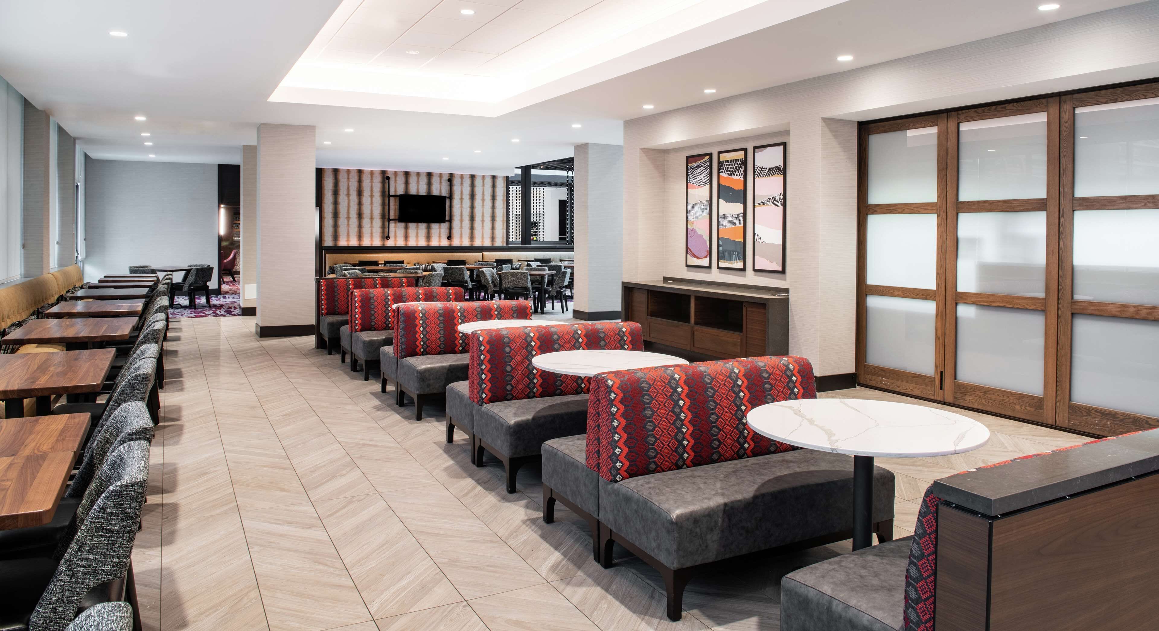 A modern restaurant with booth seating and round tables, a flat-screen TV on the wall, and abstract art on the walls.