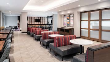 A modern restaurant with booth seating and round tables, a flat-screen TV on the wall, and abstract art on the walls.