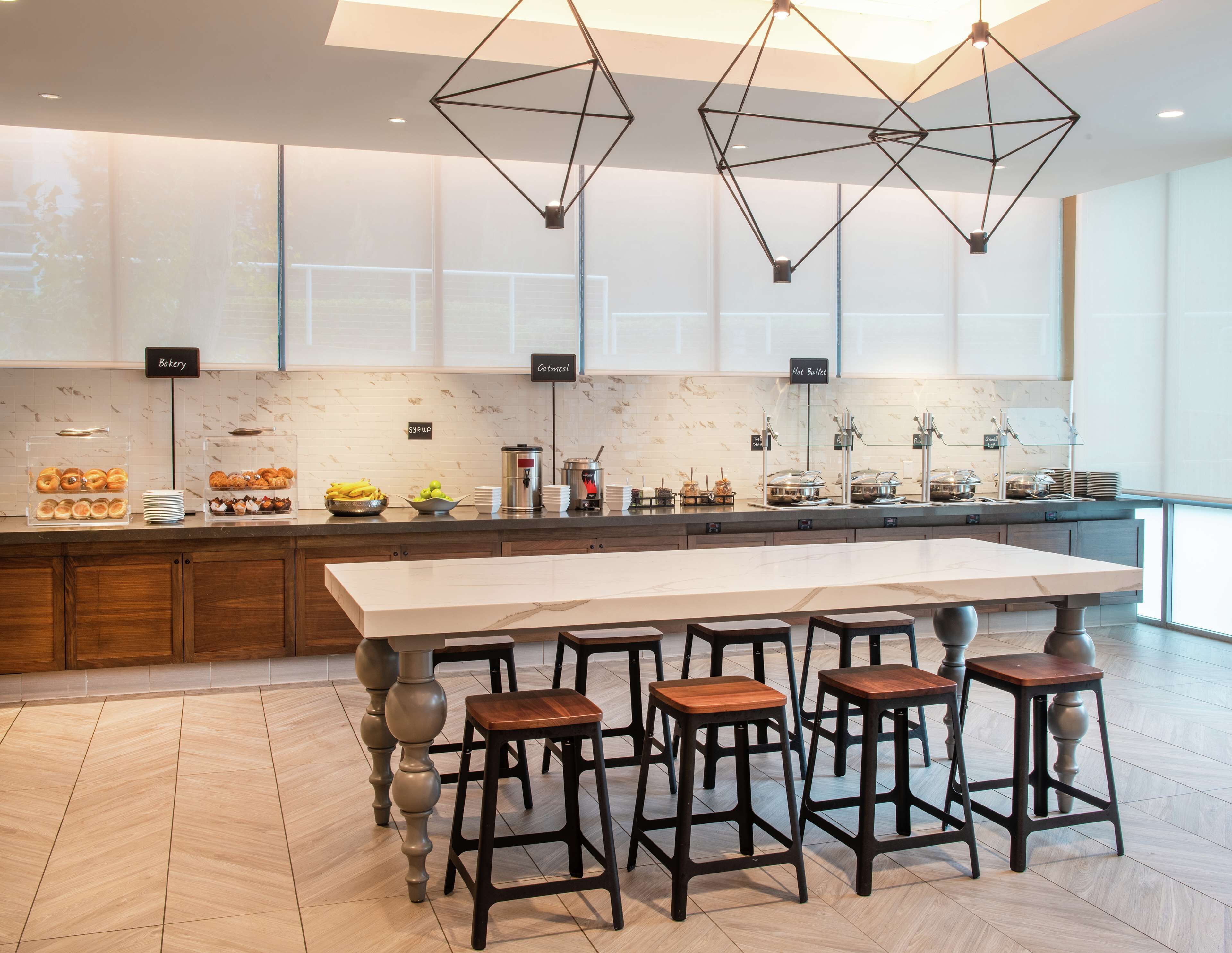 A modern kitchen with a central island, bar stools, and a breakfast buffet with labels for bakery, oatmeal, and hot buffets.