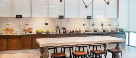 A modern kitchen with a central island, bar stools, and a breakfast buffet with labels for bakery, oatmeal, and hot buffets.