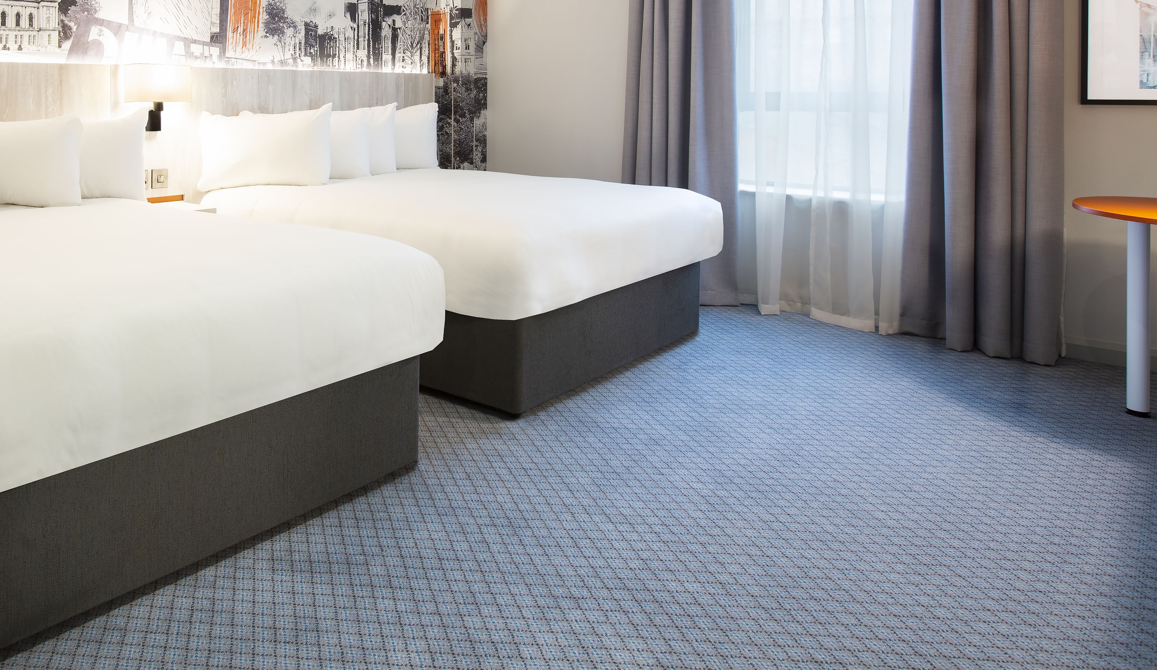 A hotel room with two beds, a small table, and a cityscape mural on the wall.
