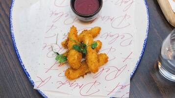 Un plato de comida rebozada y frita, adornado con hierbas, acompañado de una pequeña cazuela de salsa para mojar.