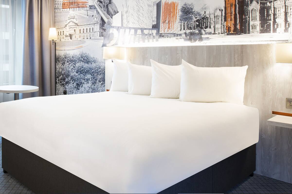 A modern hotel room with a large bed, a round table, and a wall-mounted light fixture.