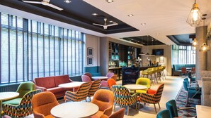 A modern lounge area with various seating options, including sofas and chairs, and a bar area with shelves of bottles.