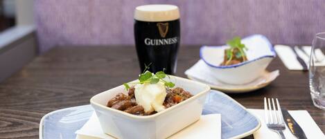 Un tazón de guiso con decoración en un plato, una jarra de cerveza Guinness y un tazón de sopa sobre una mesa.
