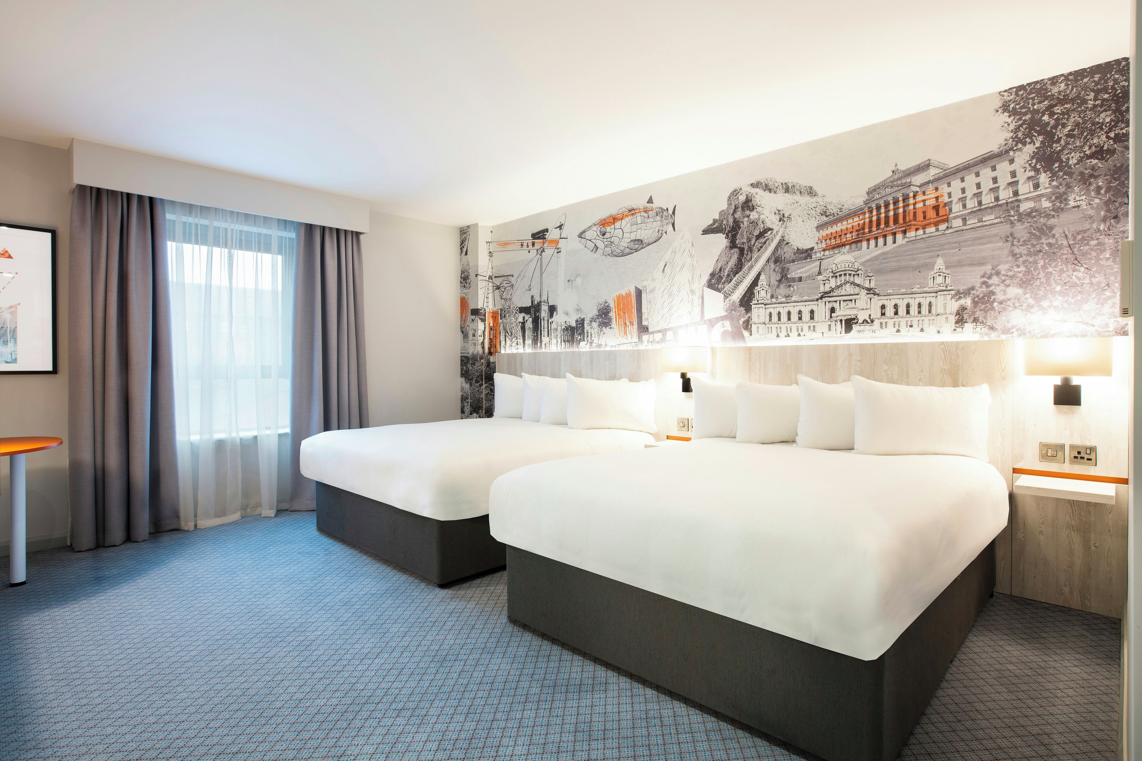Een hotelkamer met twee bedden, een grote muurschildering, een bureau en een stoel.