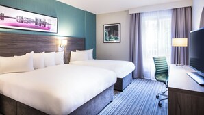 A hotel room with two beds, a desk, a chair, a TV, and a window with curtains. - Leonardo Hotel Belfast (Belfast)