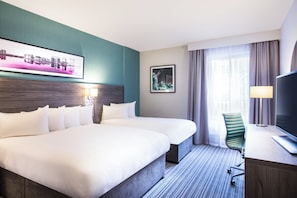 A hotel room with two beds, a desk, a chair, a TV, and a window with curtains. - Leonardo Hotel Belfast (Belfast)