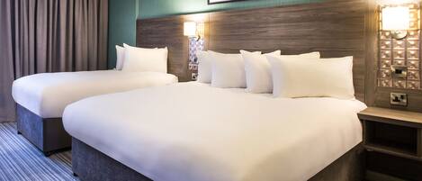 A hotel room with two beds, a cityscape picture on the wall, and a nightstand with a lamp.
