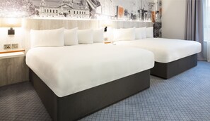A hotel room with two beds, a large mural on the wall, and a view of the city.