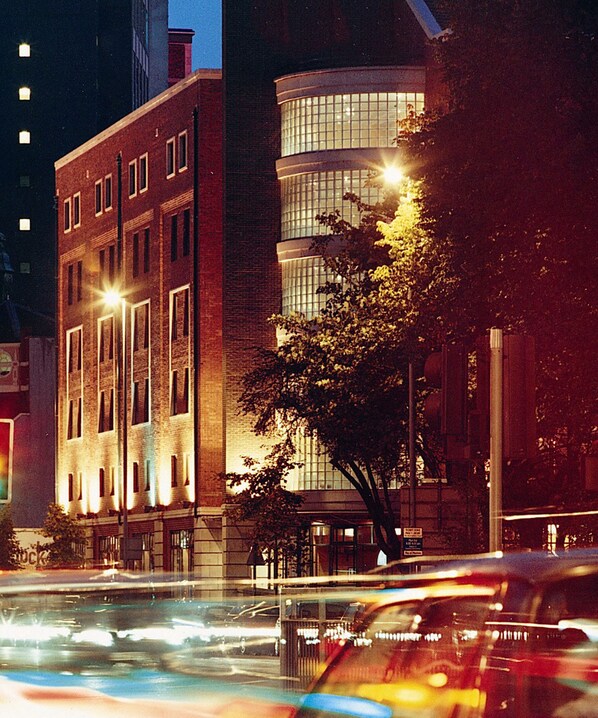 A multi-story building with a brick facade and large windows, surrounded by trees and streetlights.