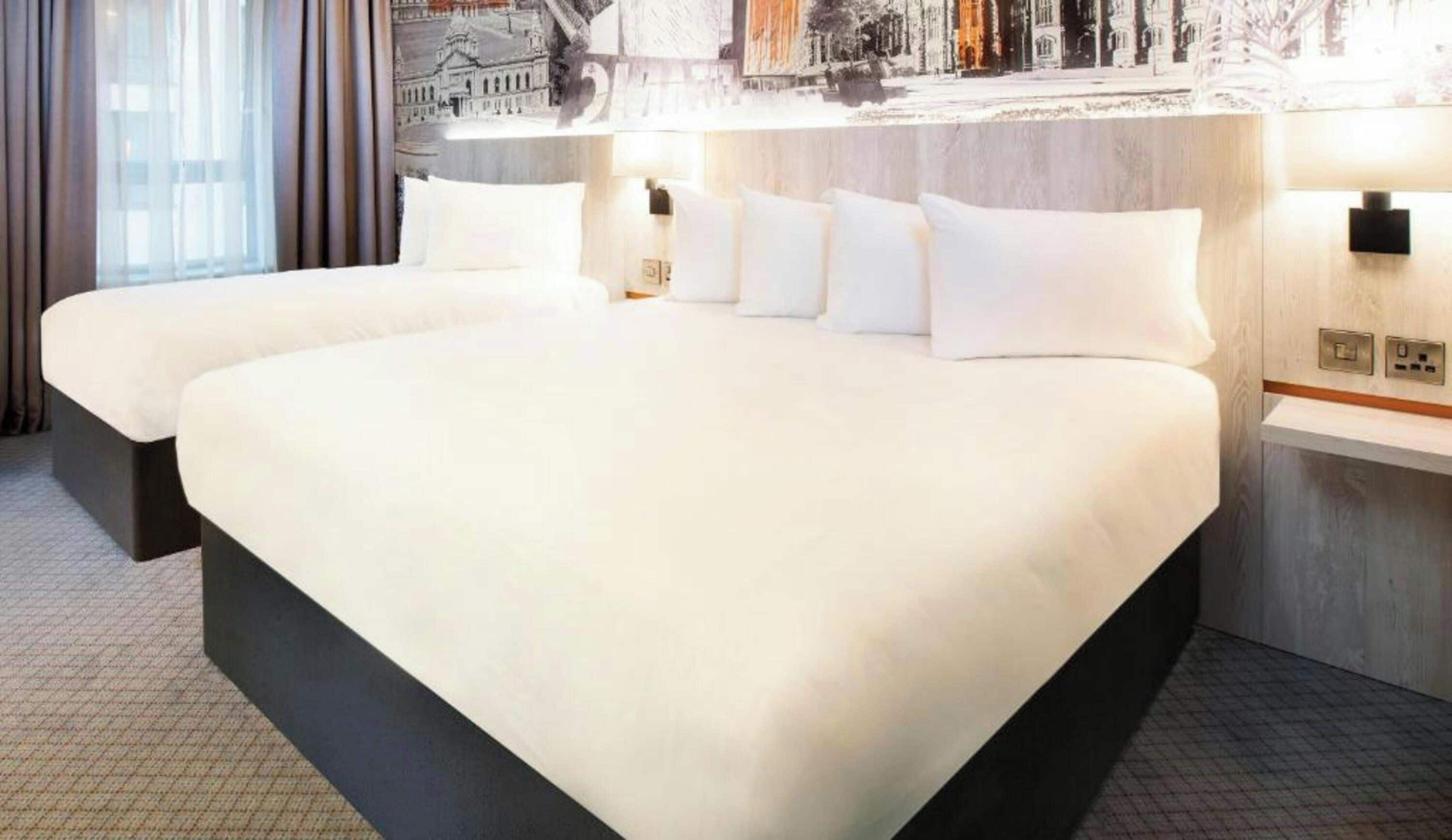 A hotel room with a large bed, a bedside table, and a wall-mounted lamp.
