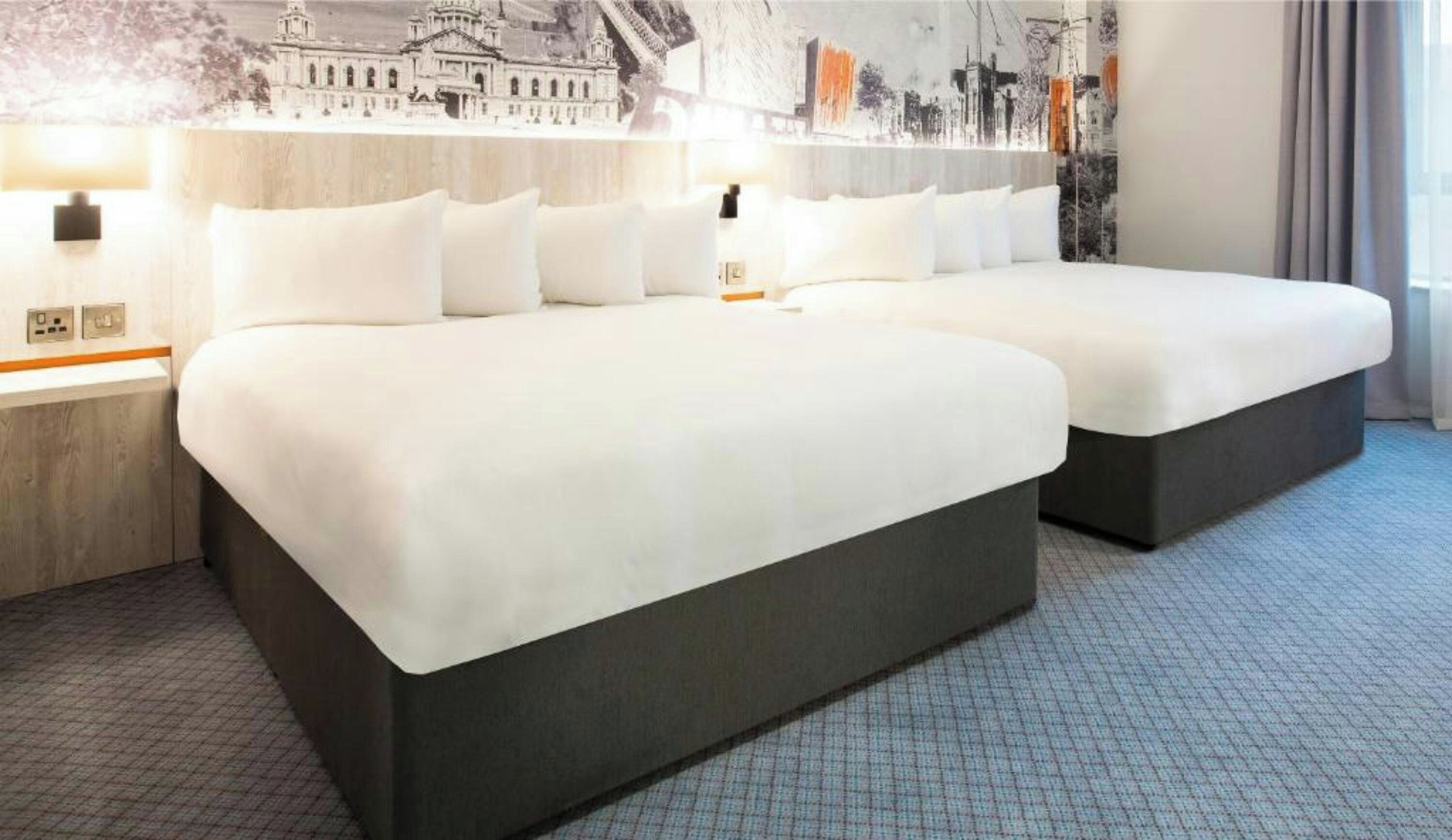 A hotel room with two beds, a cityscape mural on the wall, and a modern design.