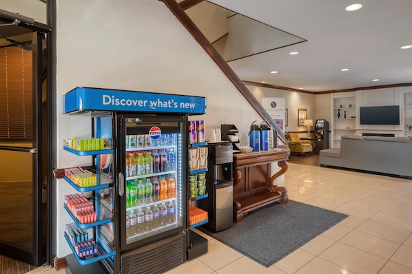 A vending machine stocked with various beverages and snacks, a coffee machine, and a seating area with a television.