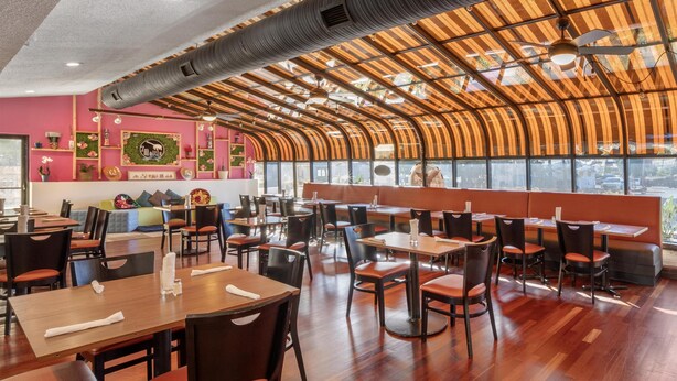 A restaurant with wooden tables and chairs, a curved ceiling, and large windows. - Best Western Battlefield Inn-Manassas (Manassas)
