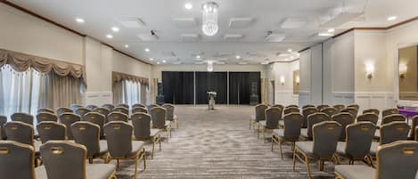 Une salle de conférence avec des rangées de chaises, un sol recouvert de moquette et un lustre.