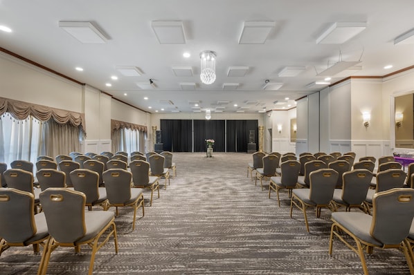 Un salón de conferencias con filas de sillas, piso alfombrado y una araña.
