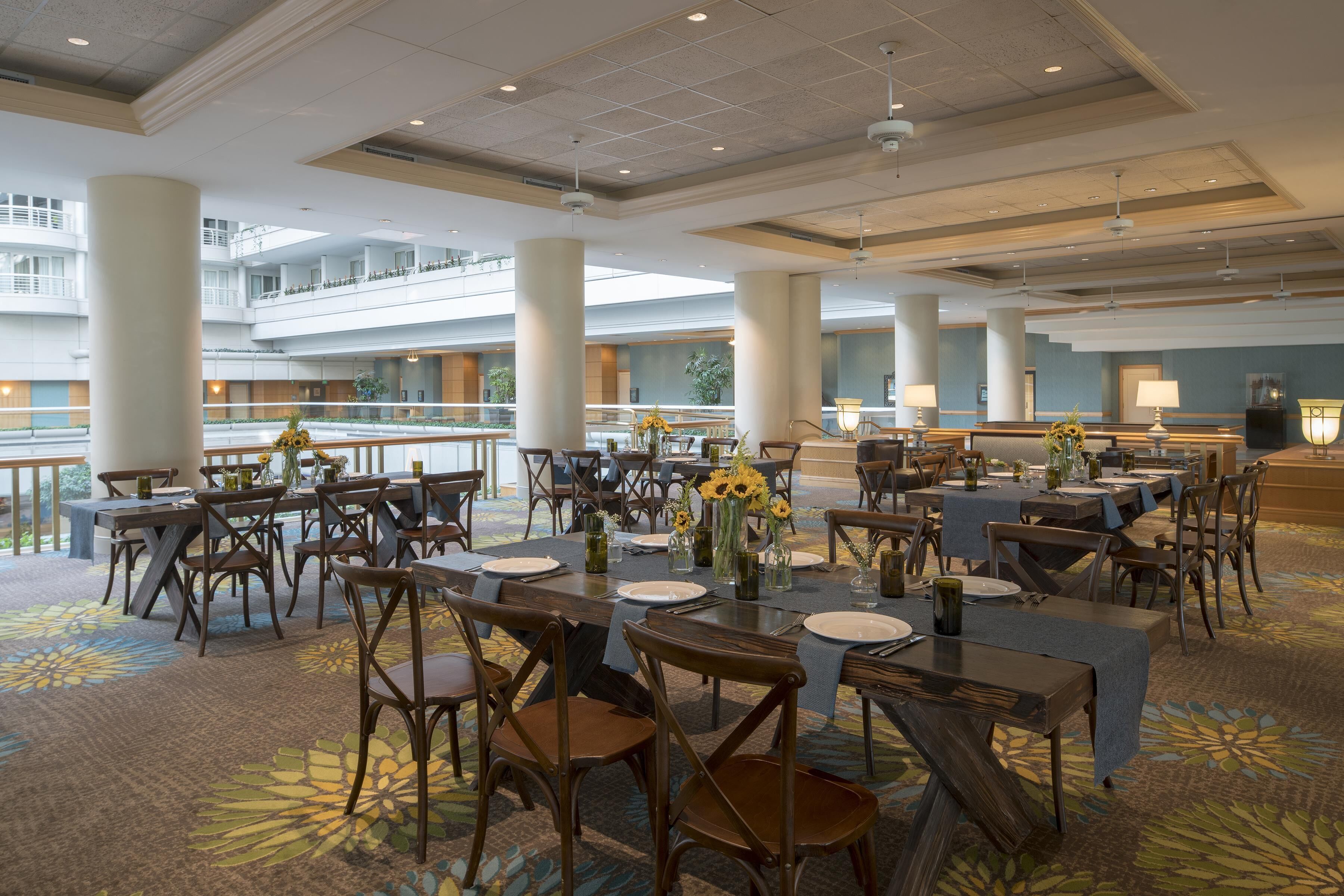 A spacious dining area with multiple tables and chairs, large pillars, and a balcony with a railing.