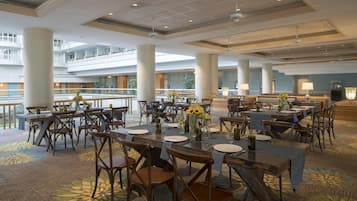 A spacious dining area with multiple tables and chairs, large pillars, and a balcony with a railing.