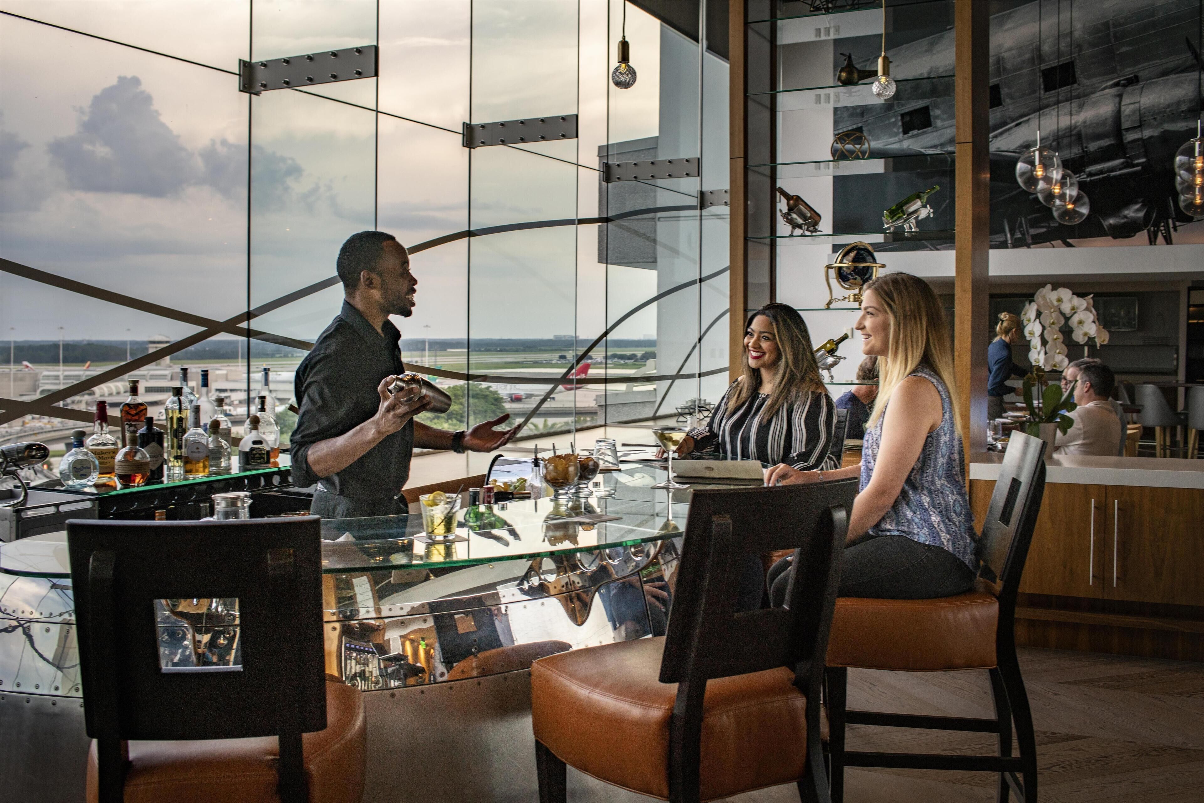 A modern bar area with a glass table, leather chairs, and a view of the airport.
