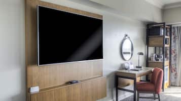 Une chambre d’hôtel dotée d’un grand téléviseur à écran plat fixé au mur, d’un bureau en bois avec une chaise, d’une petite table et d’un miroir également fixé au mur.