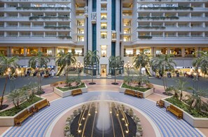 Een hotelatrium met een fontein in het midden, palmbomen en een rond zitgedeelte.