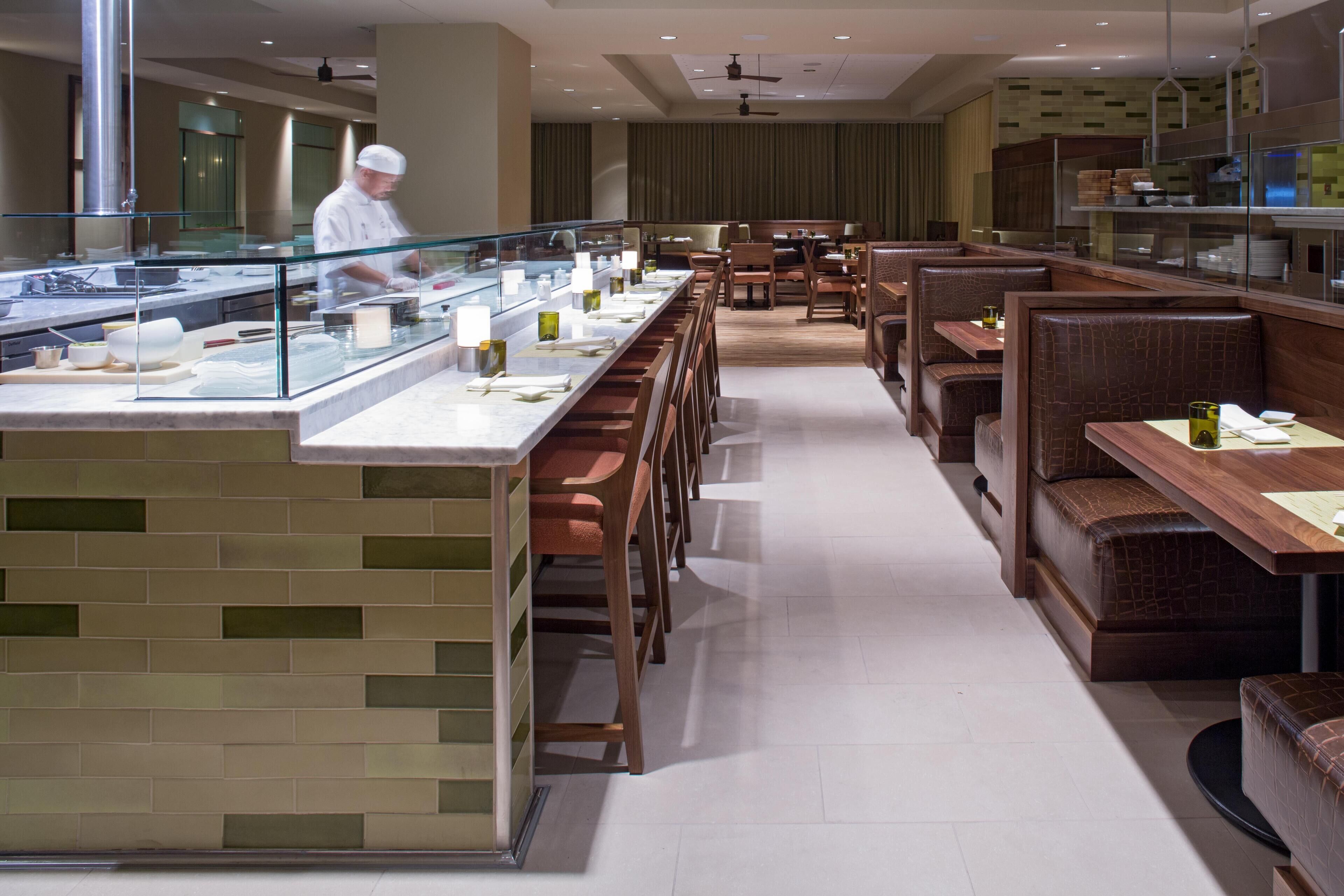 Un restaurante moderno con una barra larga, cabinas de madera y un chef preparando comida.
