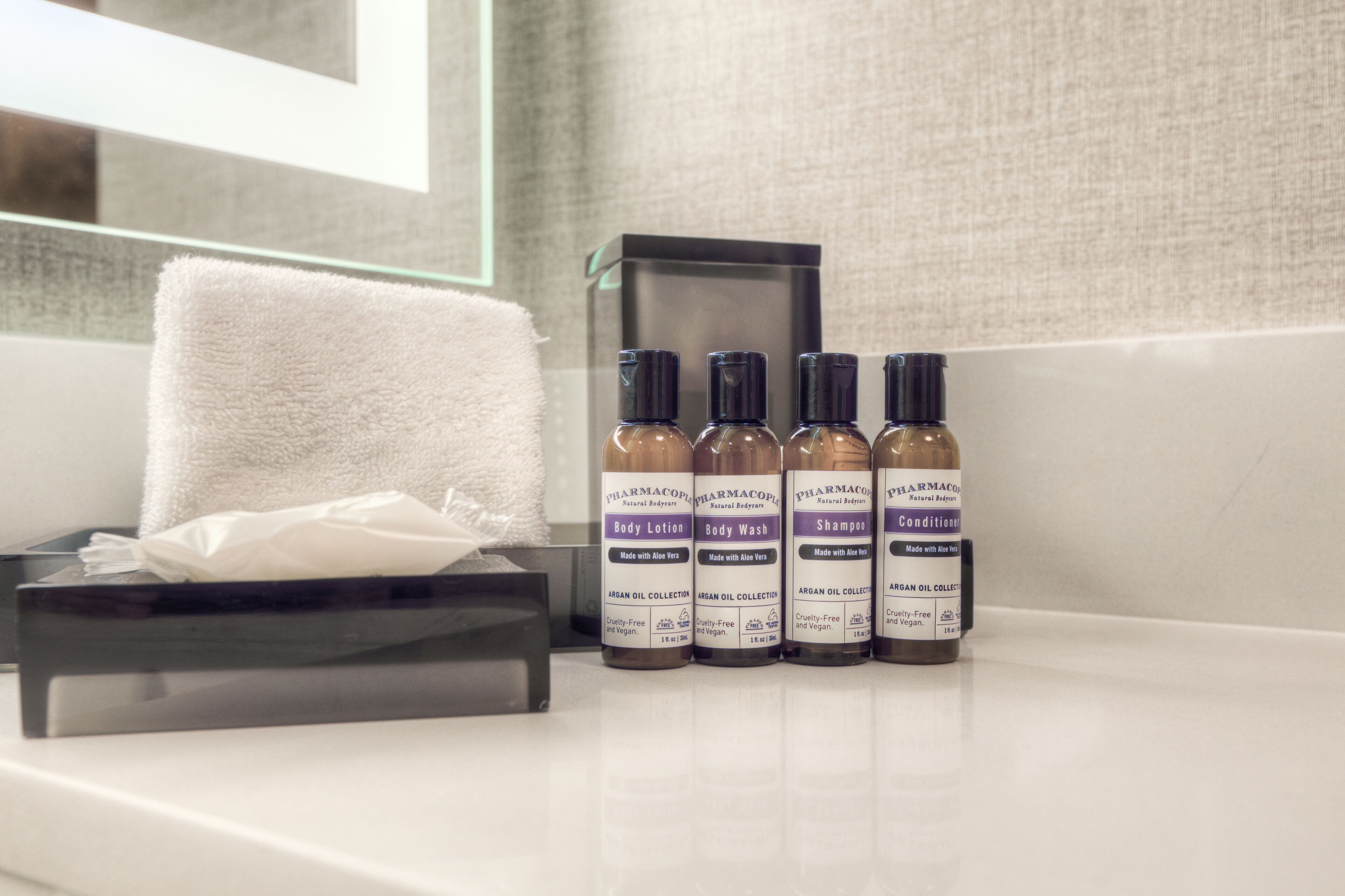 A bathroom with a white towel, a tissue box, and three bottles of body care products.