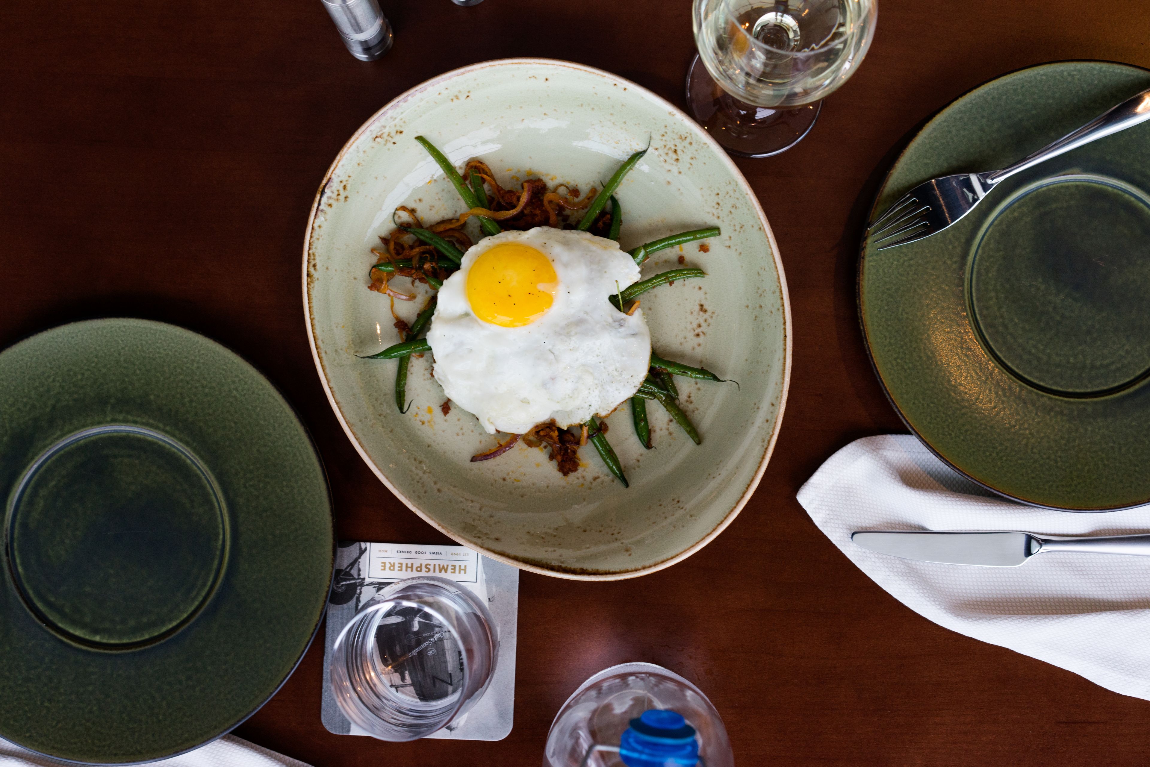 Une table à manger avec une assiette de nourriture, une bouteille d’eau, un verre d’eau et un verre de vin.