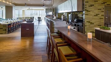 A modern restaurant with a long counter, bar seating, and a kitchen area.