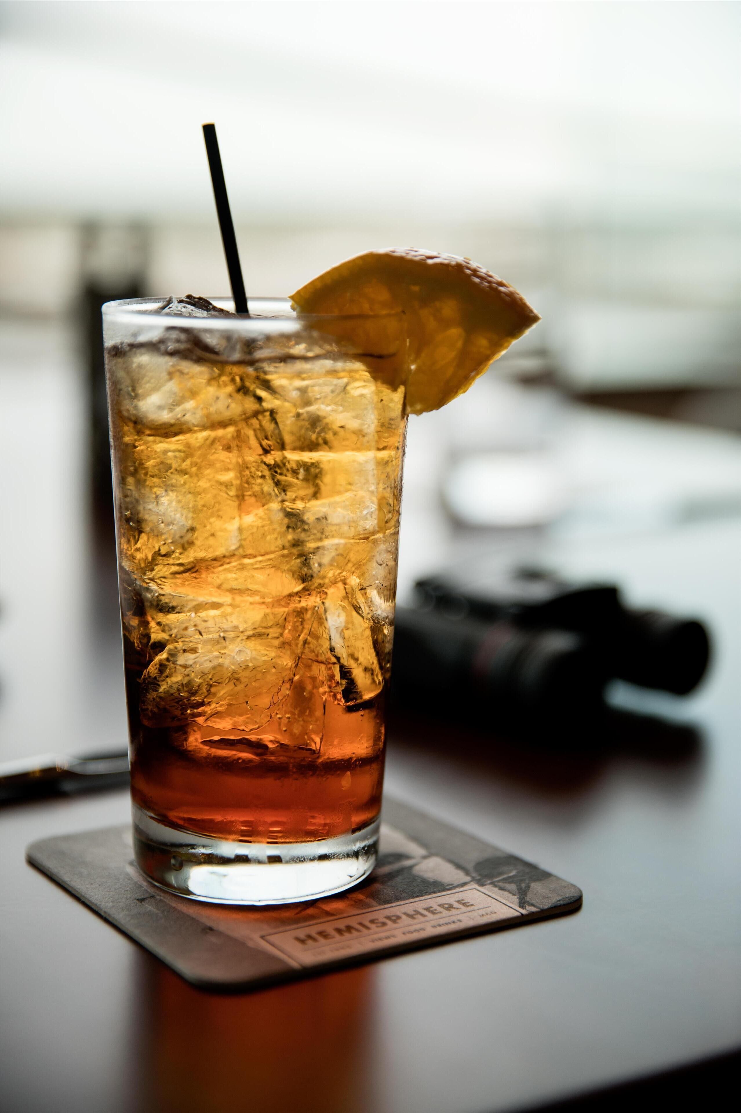 A tall glass with a straw and a slice of lemon on a coaster.