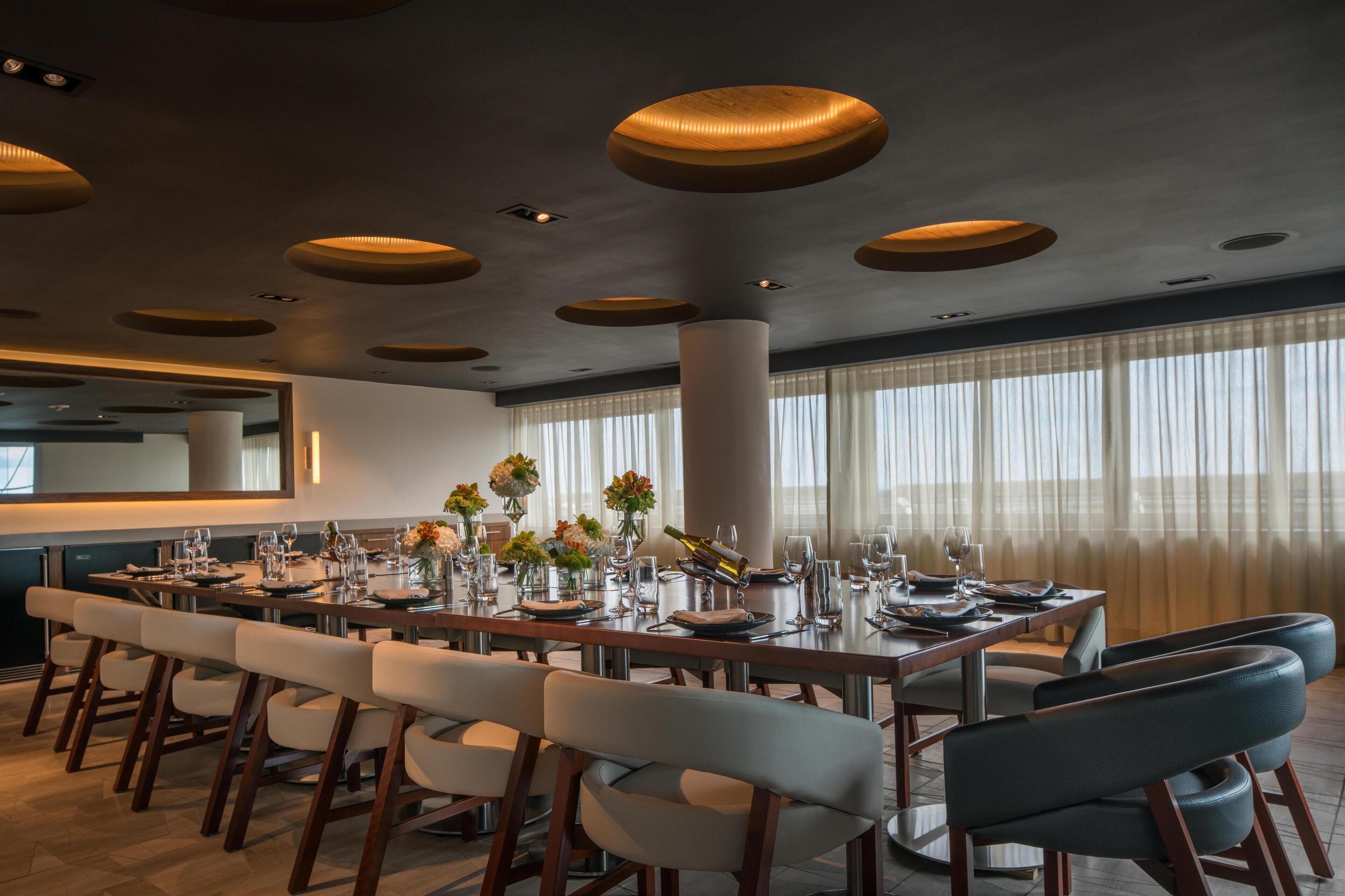 A modern dining area with a long table set for a meal, surrounded by chairs.