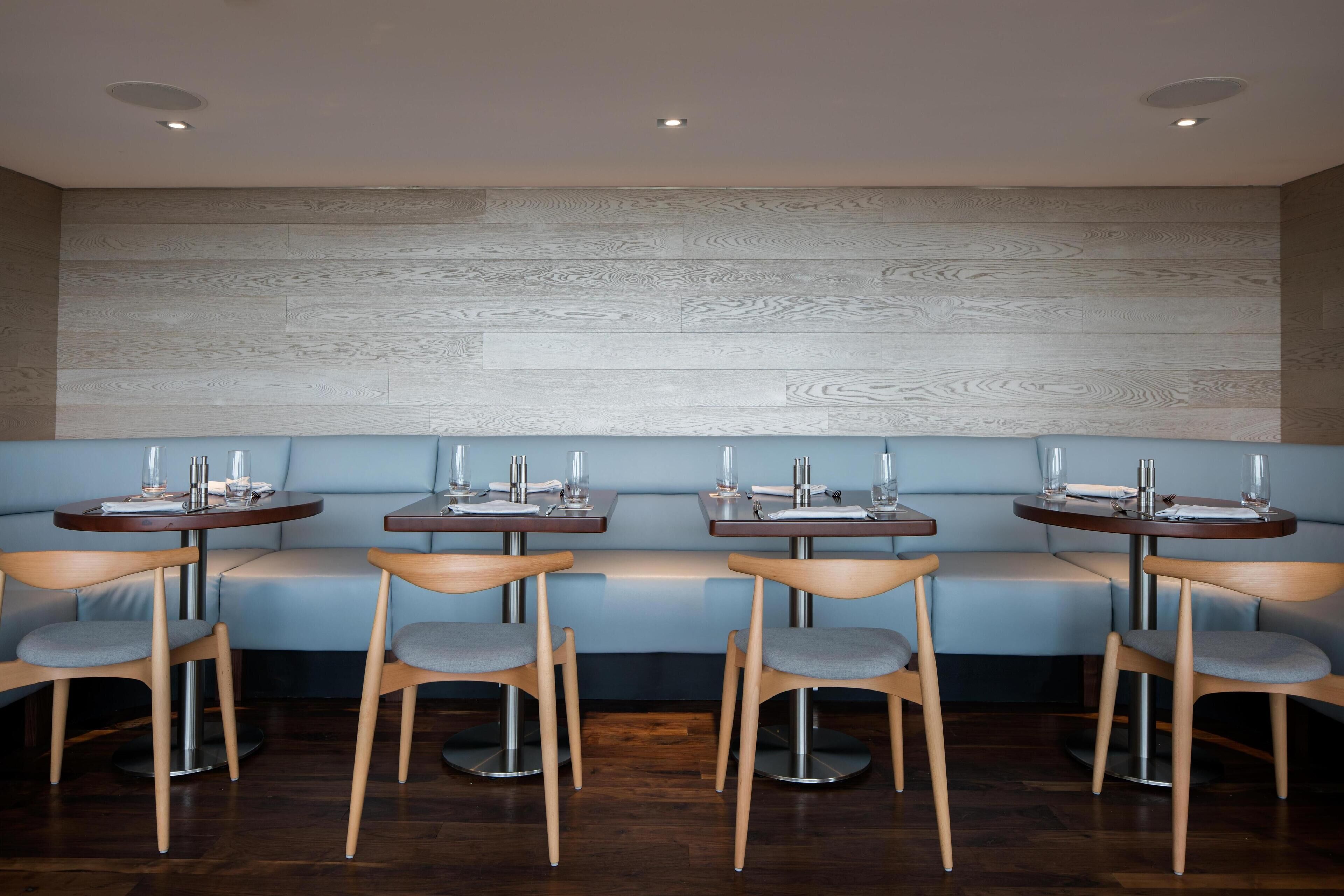 A restaurant with a blue cushioned bench seating area, wooden tables, and chairs.