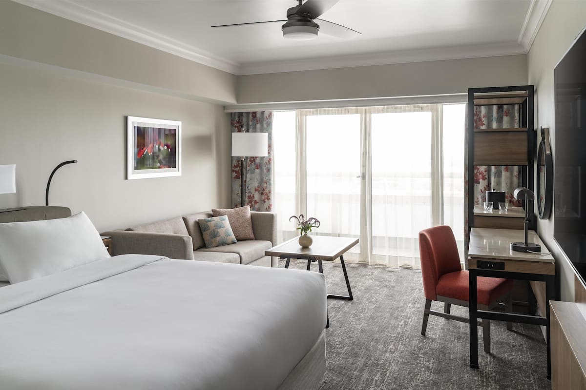 Habitación de hotel con cama, sofá, escritorio, silla, lámpara y televisor.