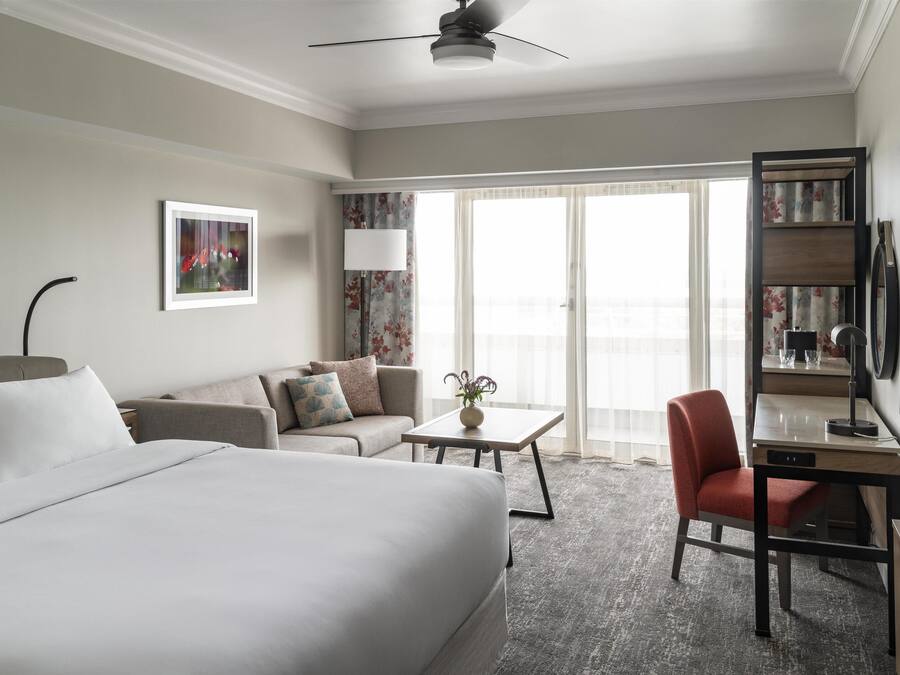 A hotel room with a bed, a sofa, a desk, a chair, a lamp, and a television.