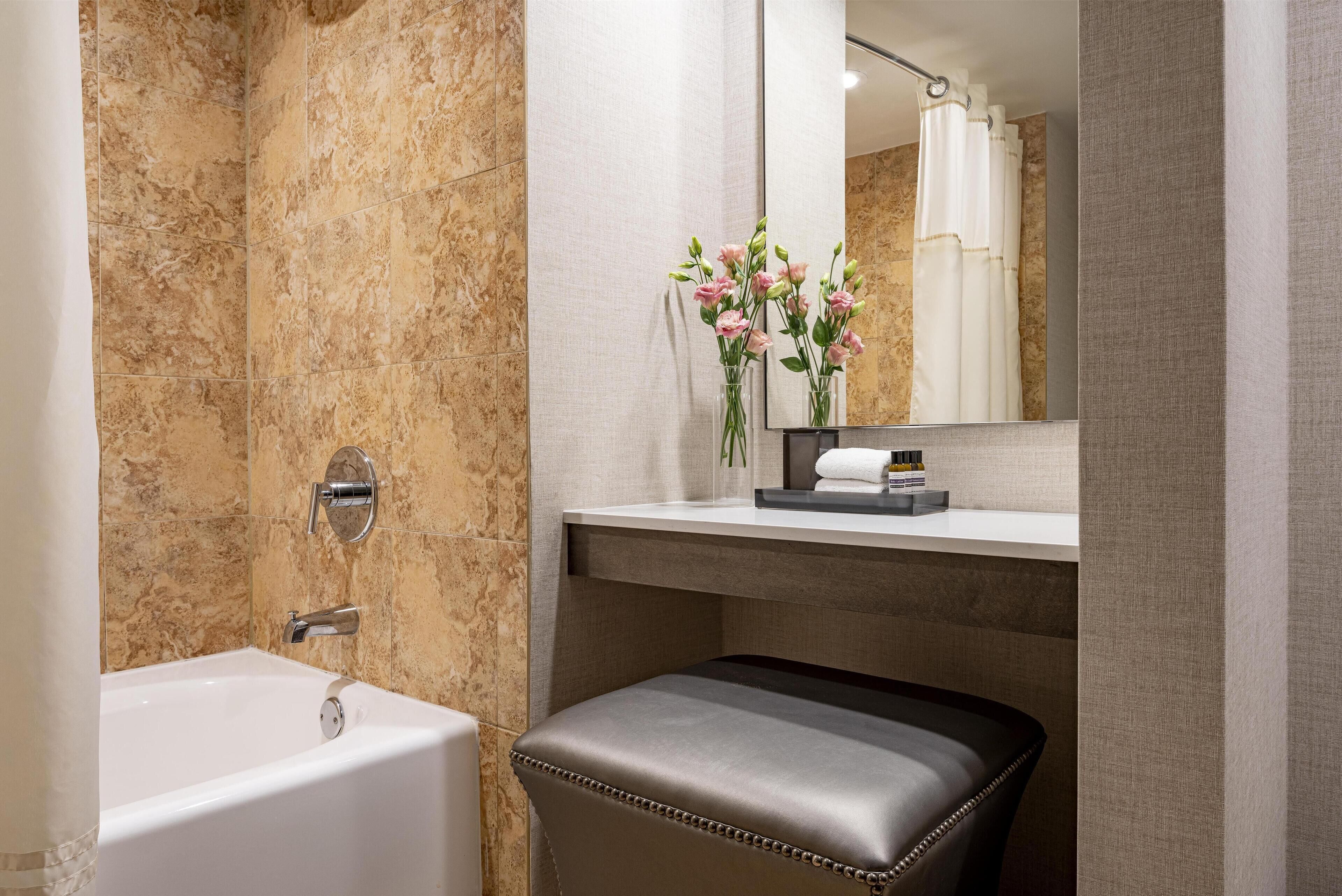 A bathroom with a bathtub, a vanity with a mirror, and a bench.